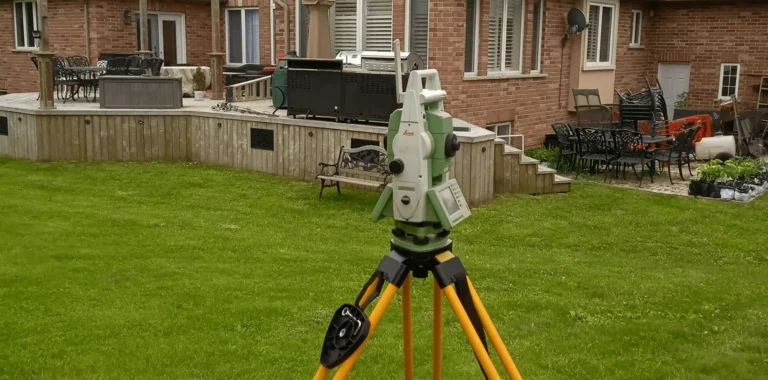 Robotic total station on an orange tripod set up on a backyard lawn for a topographic survey